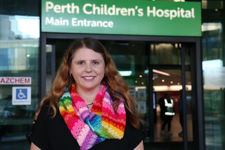 A woman wearing a multi-coloured crocheted scarf stands outside Perth Children's Hospital.