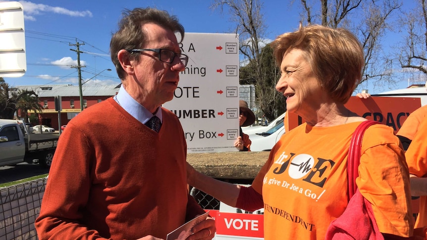 A man in a tie and jumper chats to a constituent in a campaign shirt outside a polling station.