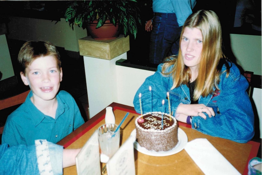 Medium shot of a boy and a girl sitting at a table with a birthday cake.
