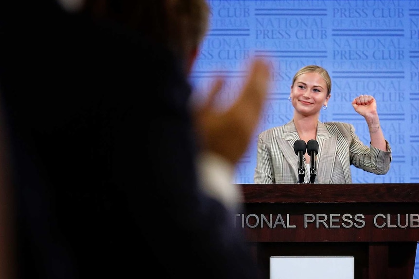 Grace Tame raises her fist as she receives a standing ovation.