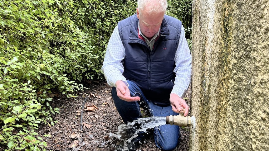 Man crouched next to water tank with water pouring out pipe 