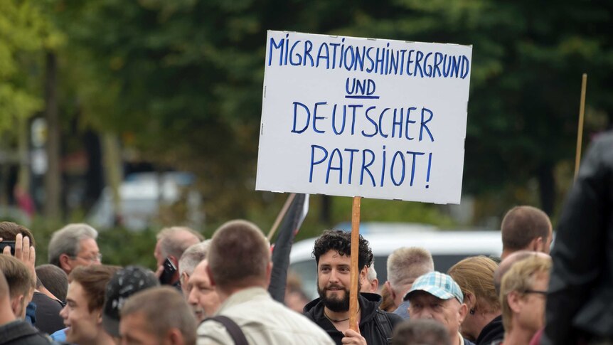 A counter-protester holds a sign which reads: "Migration background and German patriot".