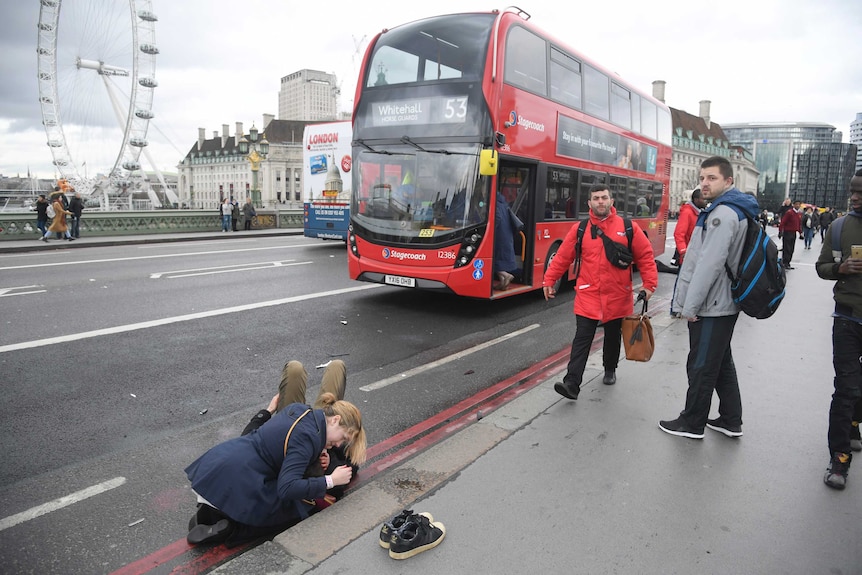 A woman assists an injured person on Westminster Bridge in London after a terrorist attack, as people stand nearby.