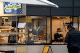 Three staff wearing face masks fill orders behind the counter of a fast food Mexican restaurant. 