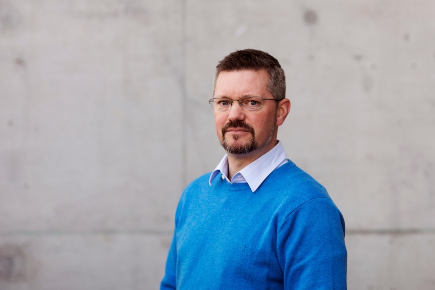 A man in a blue sweater looks neutrally in front of large concrete squares