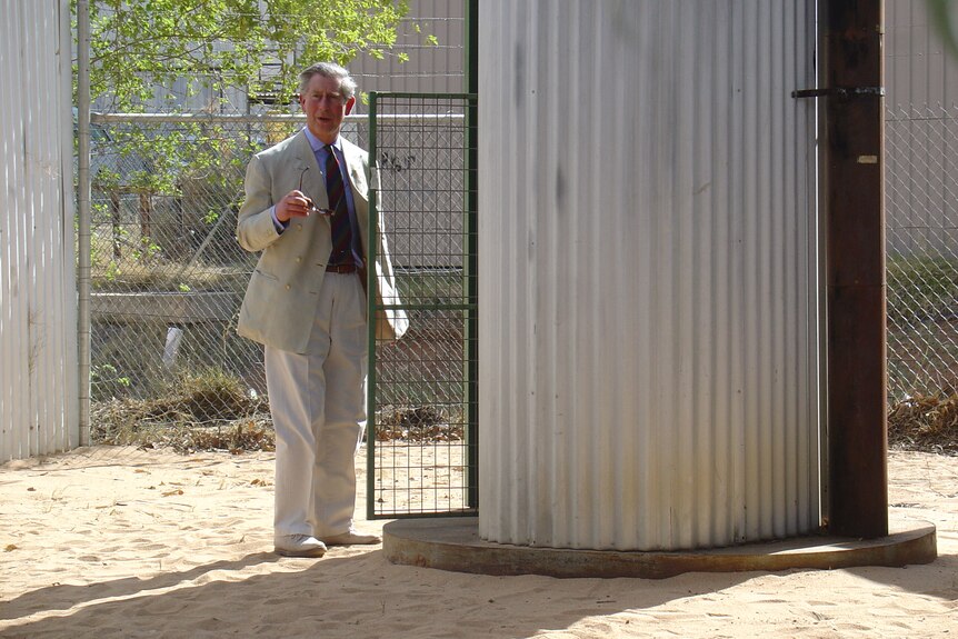 Prince Charles next to a corrugated iron building.