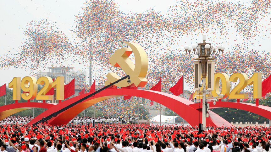 A crowd celebrates under an archway as balloons are let off in front of a giant 1921-2021 sign in Tiananmen Square.