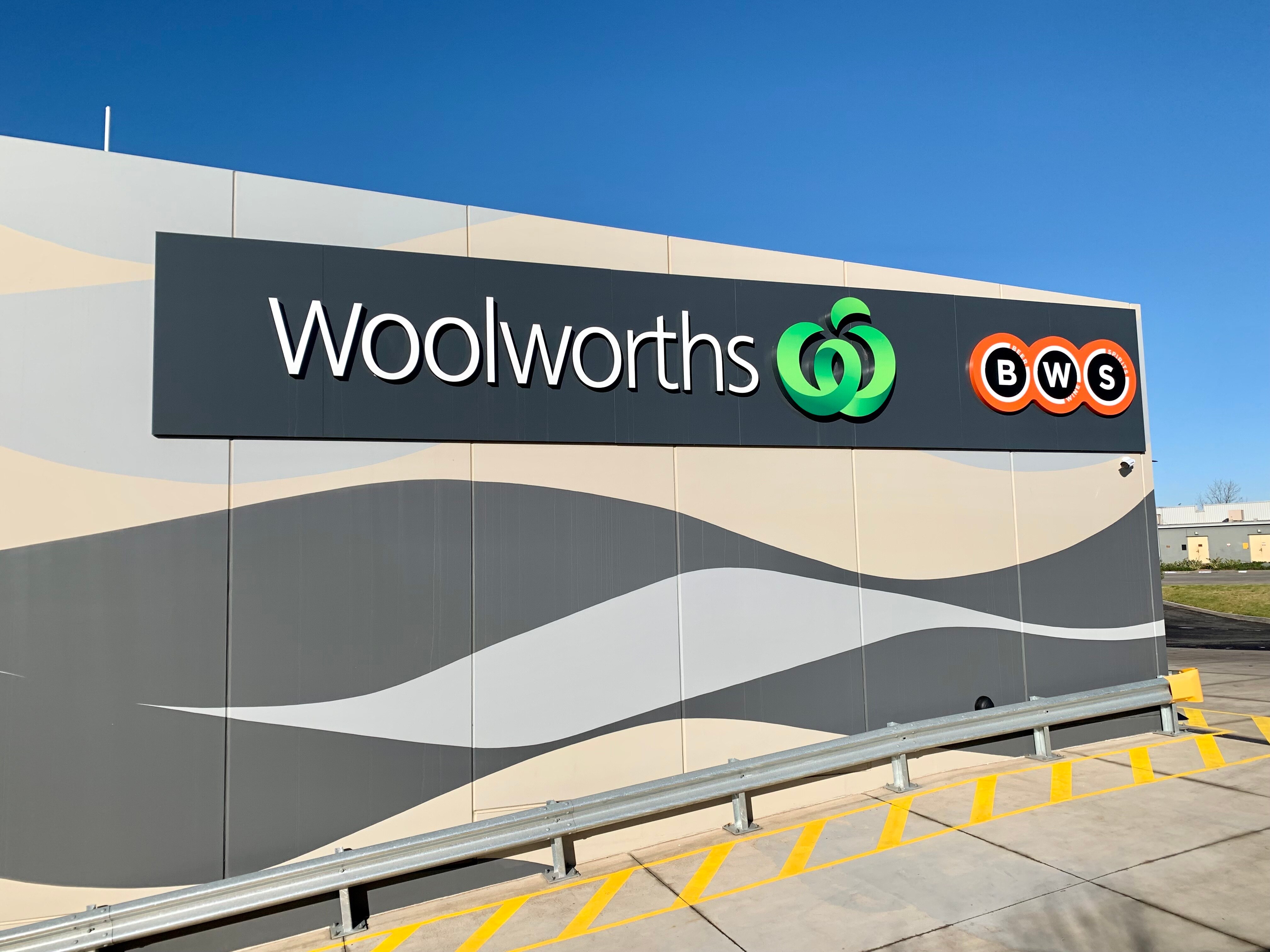 The outside of a Woolworths and BWS is a wall with signs naming the business.