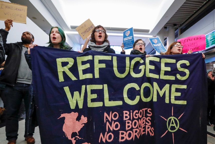 Protesers hold a large sign reading "refugees welcome, no bigots, no bombs, no borders"