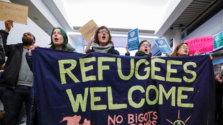 Protesers hold a large sign reading "refugees welcome, no bigots, no bombs, no borders"