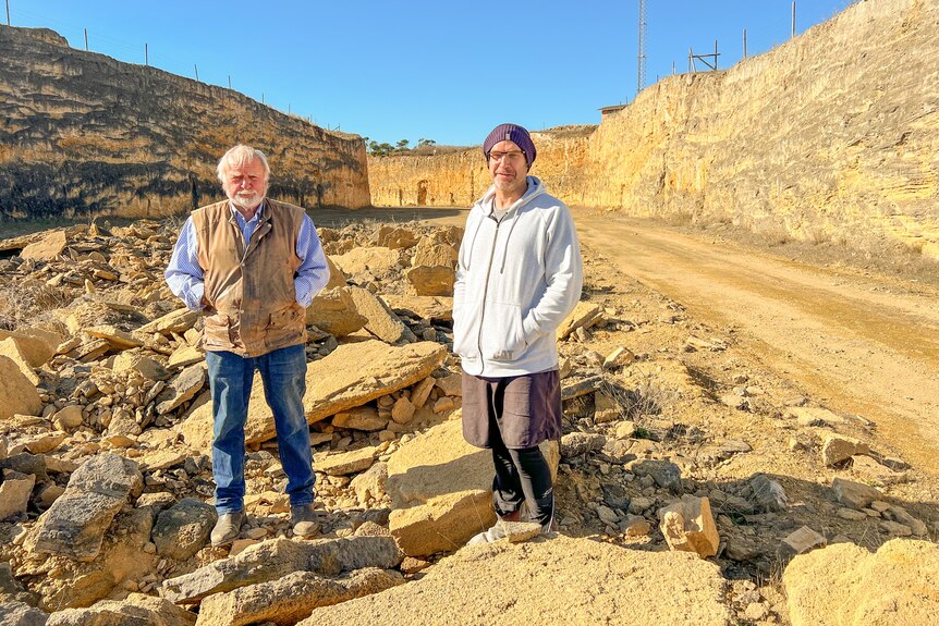 Two men in farm clothes stand on loose rock in a sandstone quarry