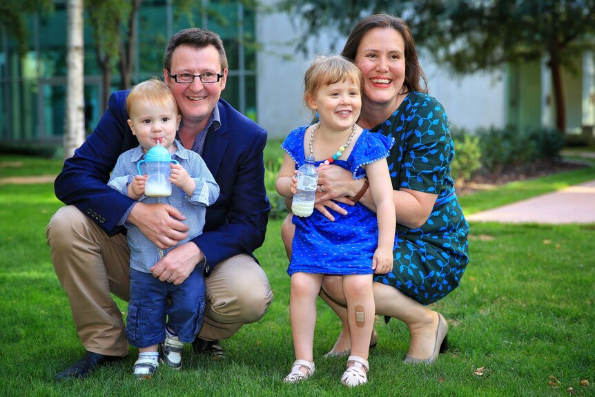 Kelly O'Dwyer wears a black dress and her husband wearing a navy jacket, kneel in a courtyard with their kids.