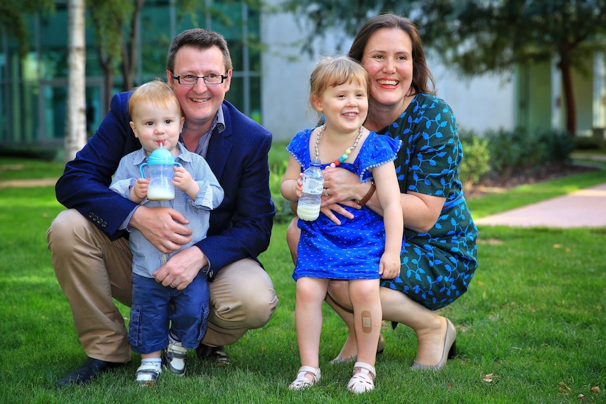 Kelly O'Dwyer wears a black dress and her husband wearing a navy jacket, kneel in a courtyard with their kids.