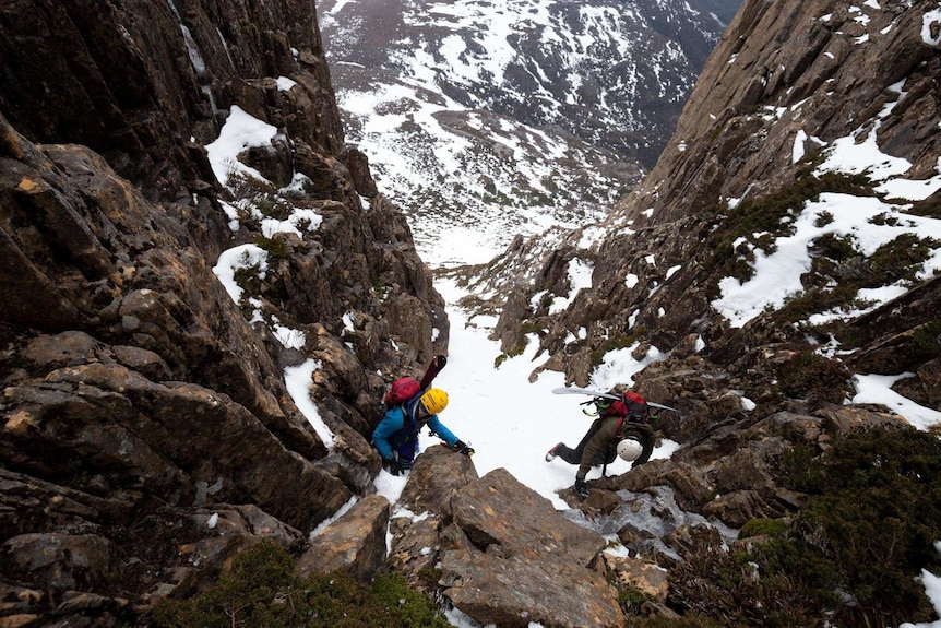 Skiers climbing over rocks