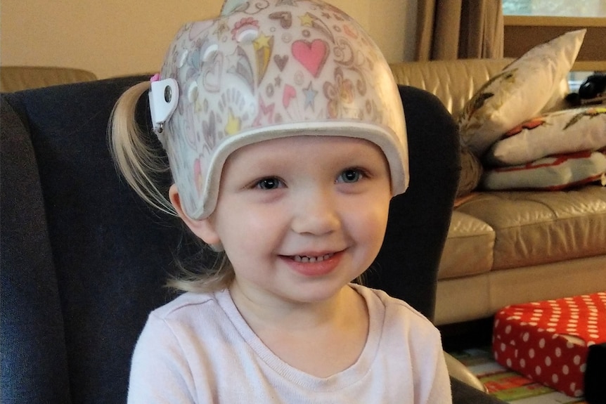 A toddler in a patterned helmet smiling widely