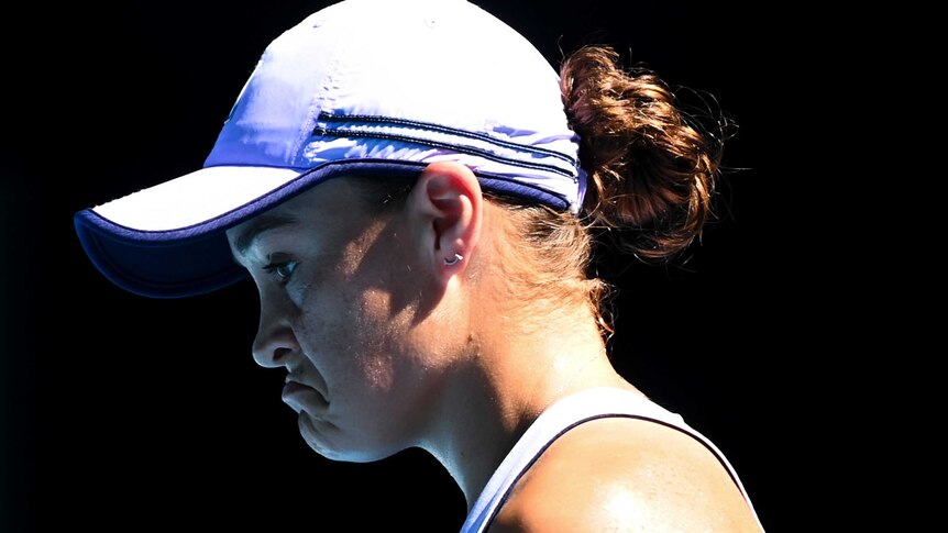 Ash Barty looks down with a downturned mouth, wearing a white peak cap