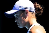 Ash Barty looks down with a downturned mouth, wearing a white peak cap