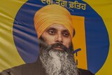 A picture of Hardeep Singh Nijjar wearing a yellow turban and black jacket on a yellow banner.