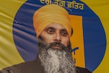 A picture of Hardeep Singh Nijjar wearing a yellow turban and black jacket on a yellow banner.