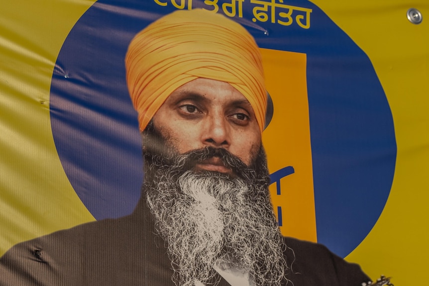 A picture of Hardeep Singh Nijjar wearing a yellow turban and black jacket on a yellow banner.