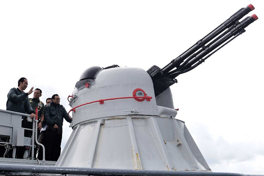 Indonesian President Joko Widodo stands behind a large weapon on a warship.