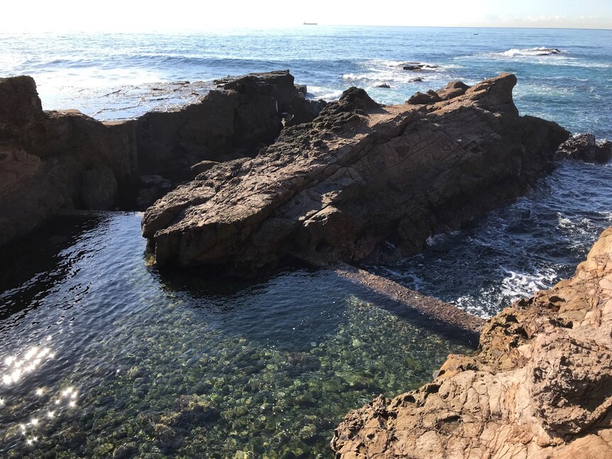 An natural ocean pool embedded among cliffs with an artificial sea wall.
