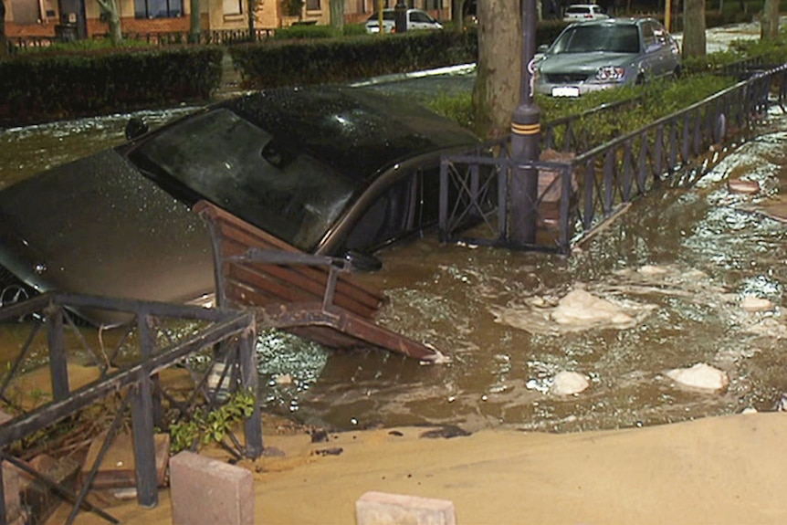 A grey car partially submerged in a hole in a suburban street. 