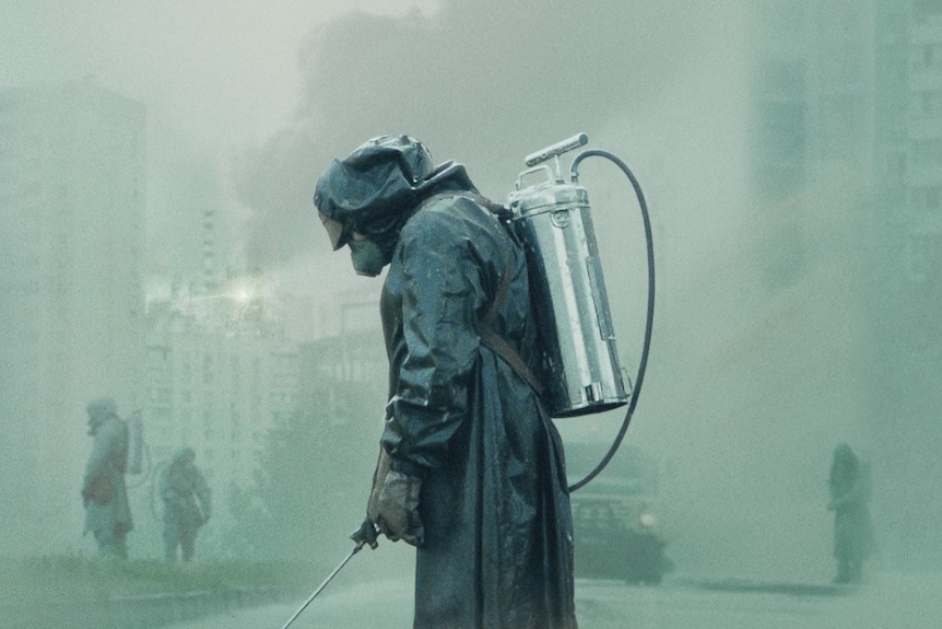 A person wearing a protective suit spraying the ground. The air is thick with smoke with a hint of a green tinge.