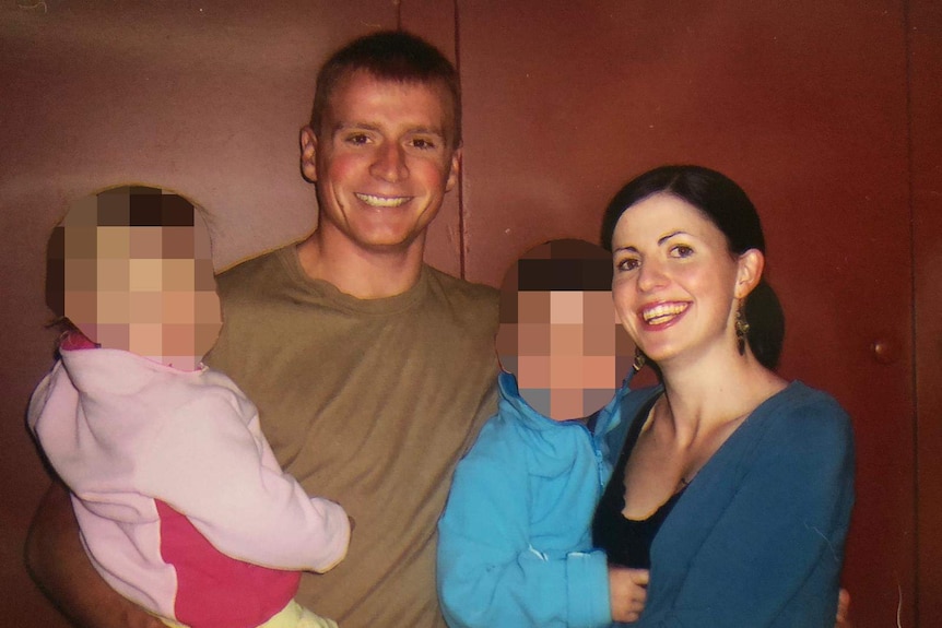 Family photo of two young children being held by smiling man in t-shirt and mother in blue cardigan