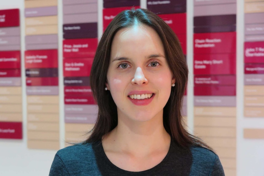 Eugenie Prior, a researcher in population health stands in front of board with red writing on it.