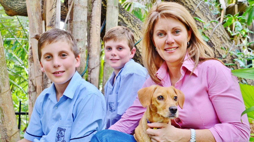 Tracey Hayes sitting with two of her sons and their dog on her lap with green bushland in the background.