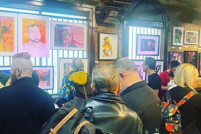 Men stand in a pub surrounded by art work.