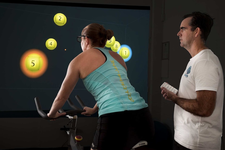 Woman on exercise bike while coach monitors performance.