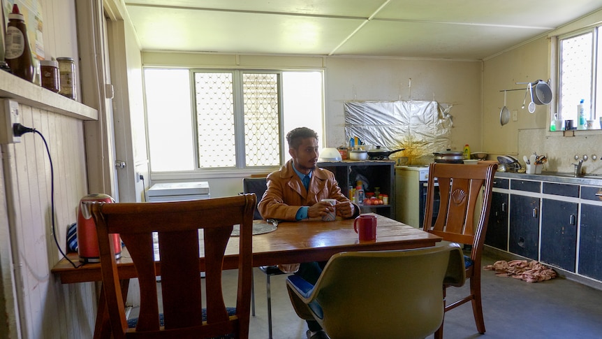 Hussain sitting at a table in the kitchen of an old Queenslander-style cottage in Gatton, June 2022.