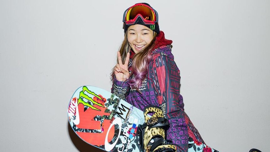 Chloe Kim suited up in her snowboarding gear giving the peace sign.