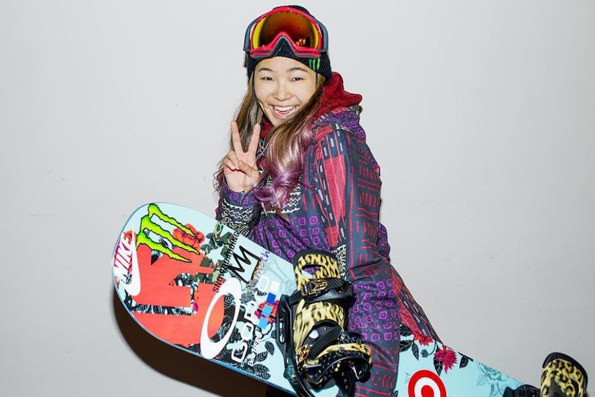 Chloe Kim suited up in her snowboarding gear giving the peace sign.