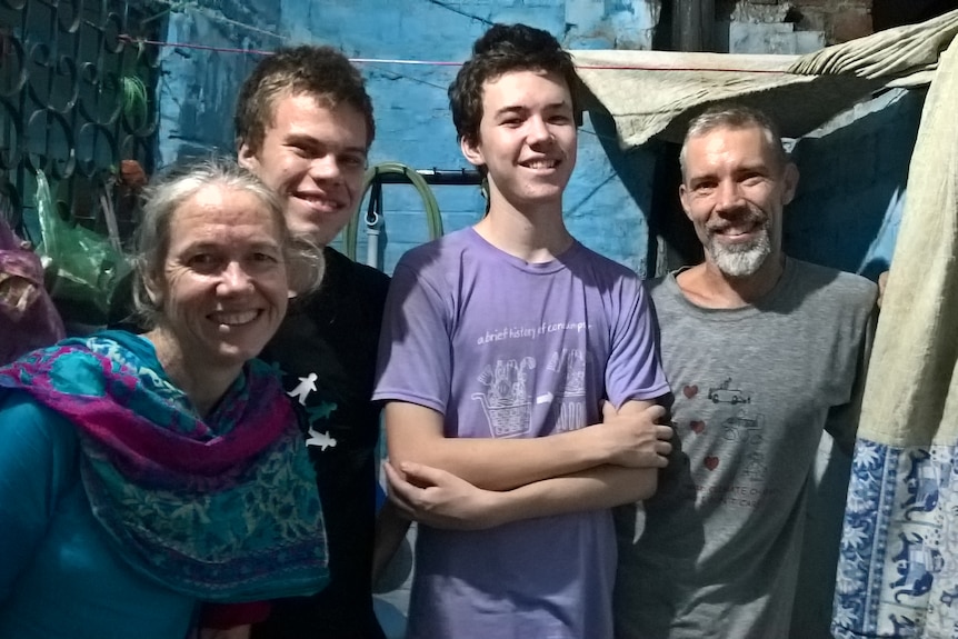 Two young adult men, one man with facial hair and one lady with hair pulled back smile facing the camera in slum area.