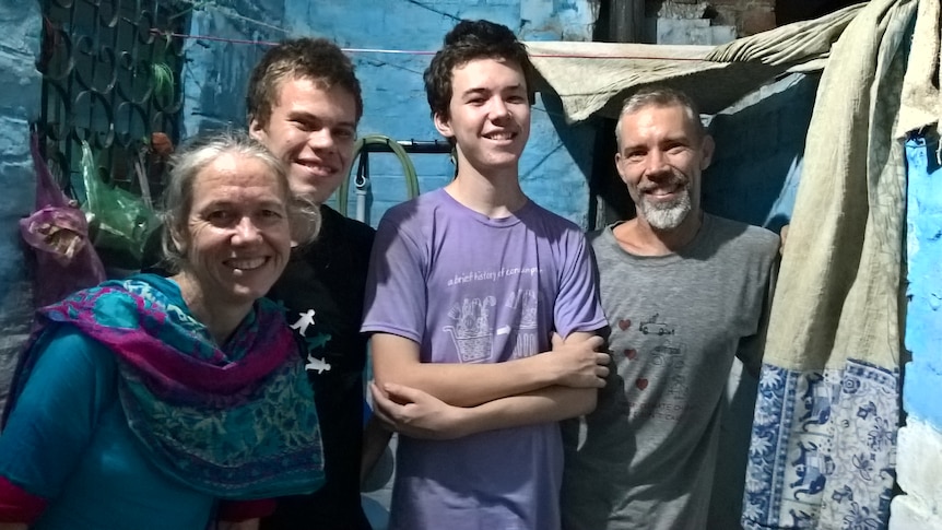 Two young adult men, one man with facial hair and one lady with hair pulled back smile facing the camera in slum area.