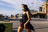 Pedestrians wearing masks cross the road in front of Flinders Street Station in Melbourne