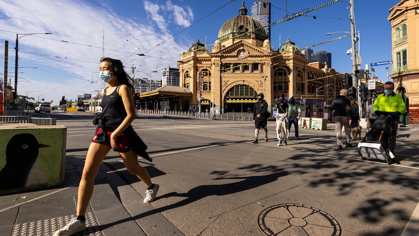 Pedestrians wearing masks cross the road in front of Flinders Street Station in Melbourne