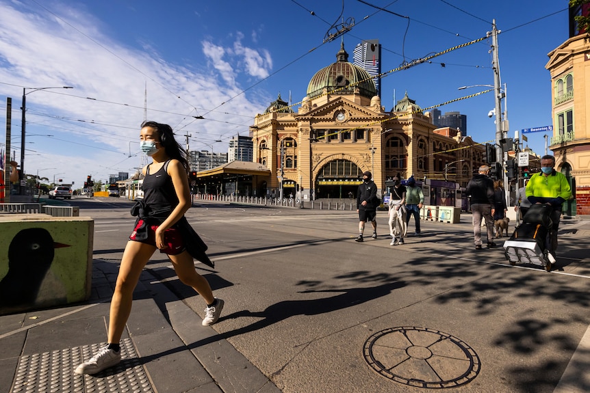 Pedestrians wearing masks cross the road in front of Flinders Street Station in Melbourne