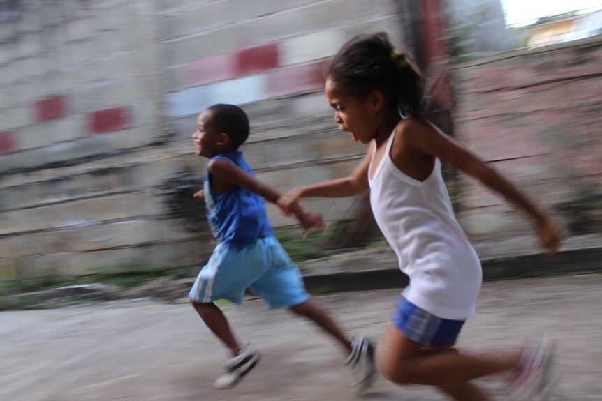 Girl and boy running beside a grey wall