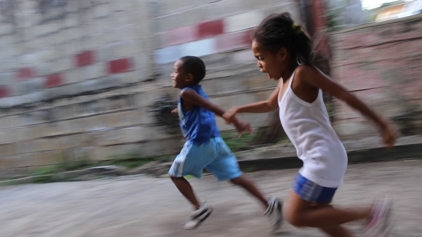 Girl and boy running beside a grey wall