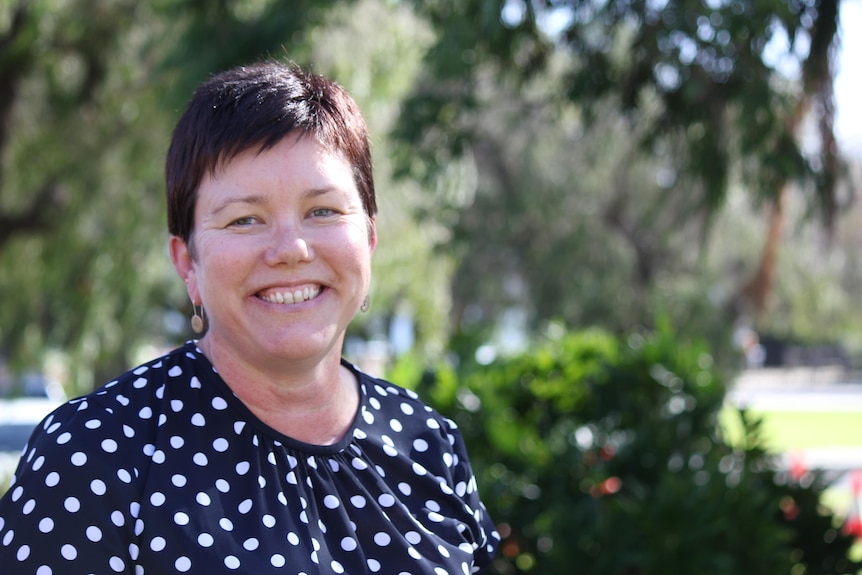 A smiling women in a polka dot navy white top.