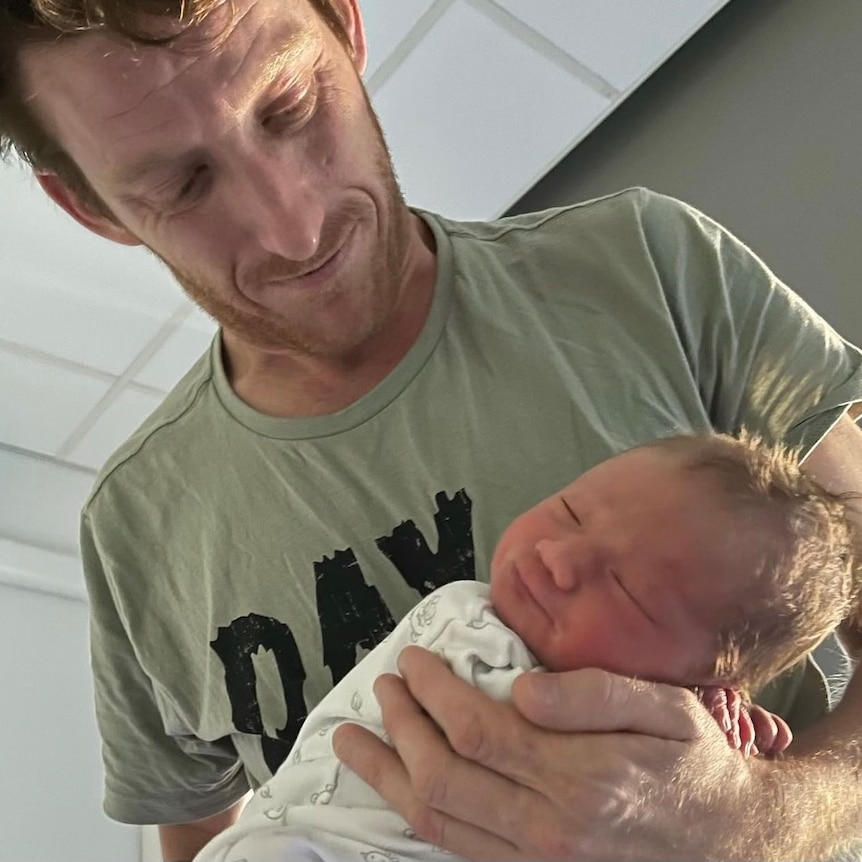 A man looks down lovingly at a newborn baby in his arms. 