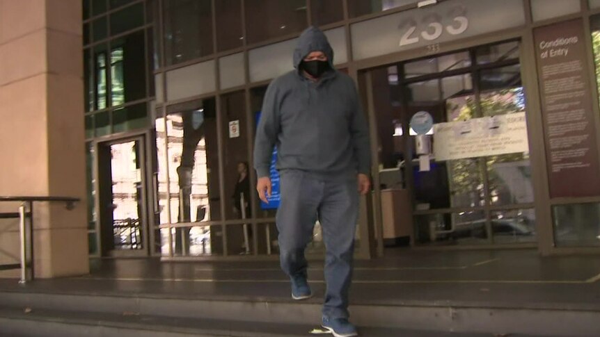 A man in a mask and a hoodie walks away from a court building.