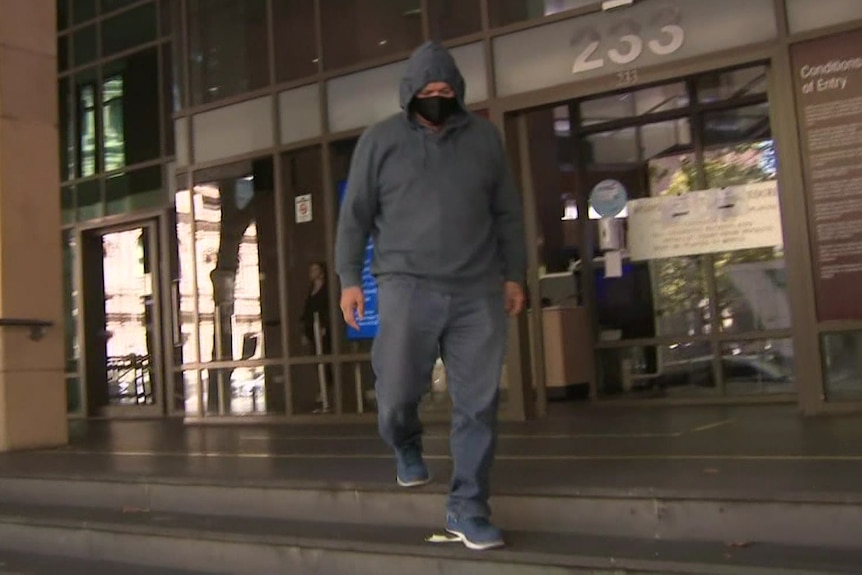 A man wearing a face mask, jeans and a blue hooded jumper leaves court.