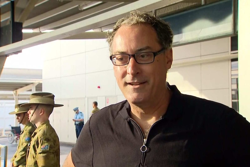 A man standing at the airport with an army soldier to his left.