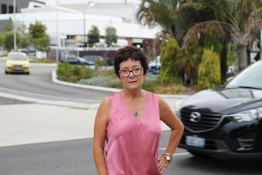 woman standing with hand on hip in front of shopping centre with car passing