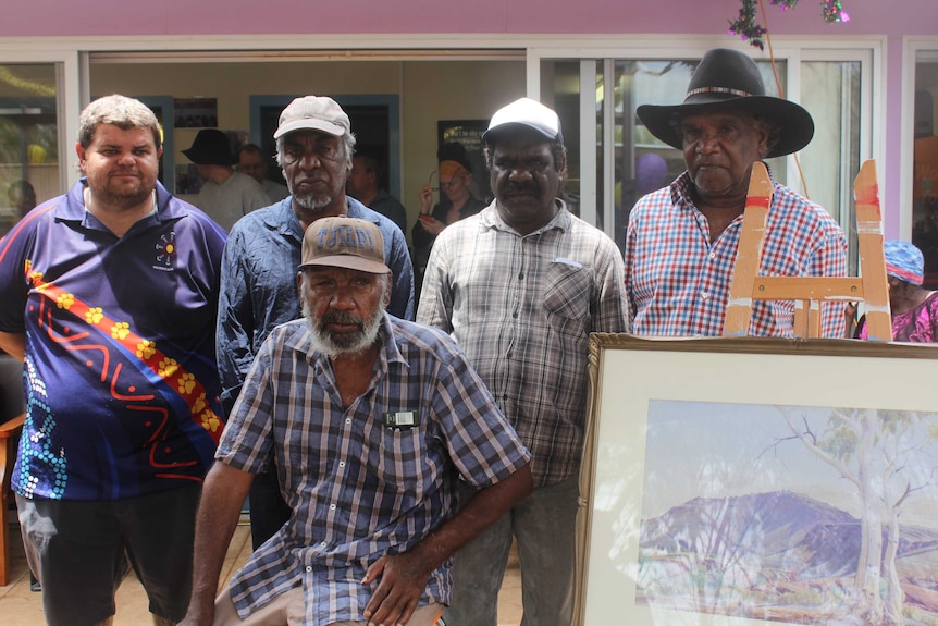 Five board members of the Ngurratjuta Aboriginal Corporation stand with the Albert Namatjira painting on an easel.